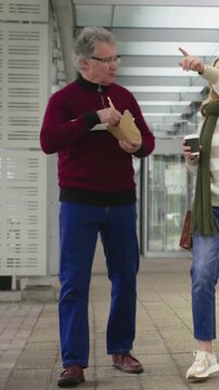 Vertical video: Walking couple talking man eating box chopsticks under roof woman scarf holding cup