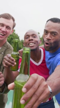 Vertical video: Raising green bottles, man in red jersey starting toast by pool, men tending grill