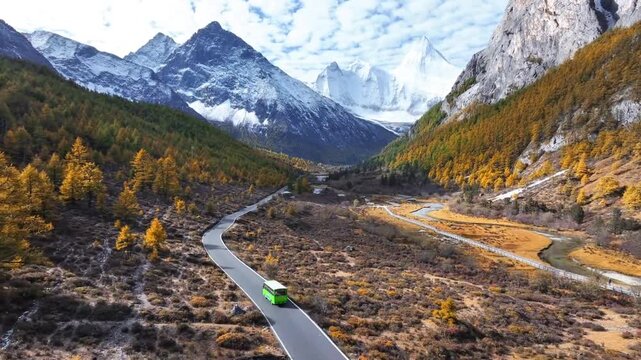 Aerial view of green tourist bus driving on valley road under snow peak in Daocheng Yading China