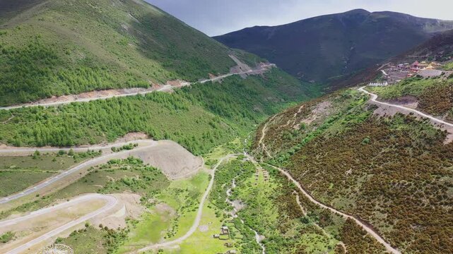 Aerial view of scattered mountain dirt roads on layered green hillside in Daocheng Yading China