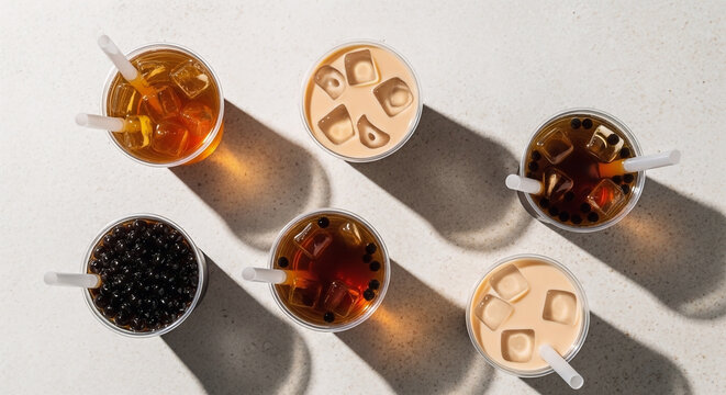 A top-down view of a variety of refreshing iced drinks, including different types of bobba tea with chewy tapioca pearls and milk, captured in studio.