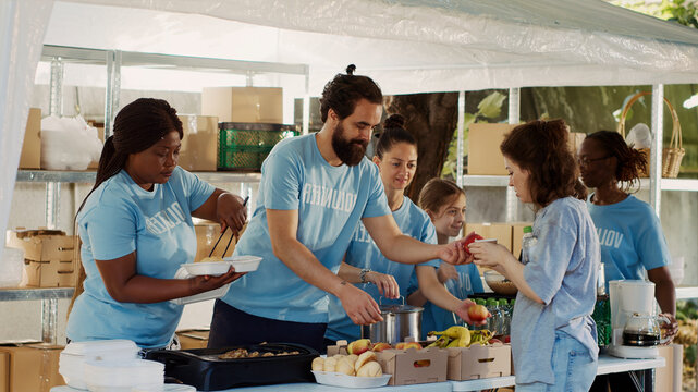 Young people united by commitment to charity, aiding underprivileged and contributing food to individuals experiencing homelessness, volunteers sharing free meals to the poor and needy.