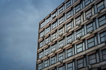 Fototapeta premium Brutalist office building in Belgrade in Serbia with concrete facade, grid windows, exterior air conditioners and stormy sky, reflecting communist era urban architecture and city offices.