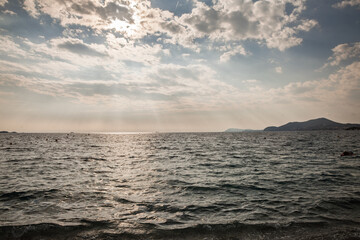 Obraz premium Panoramic view of the Mediterranean Sea off Hyeres on the French Riviera, in france, sunlit clouds, distant coastline, small buoys, hazy horizon and textured waves along the shore in southern France.