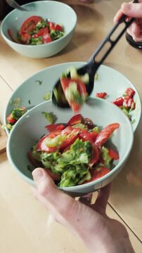 hand serving salad, salad in bowl, black utensil, serving spoon, tossing salad, mixing greens, bowl of salad, fresh vegetables, green leaves, cherry tomatoes, cucumber slices, red onion rings, salad 