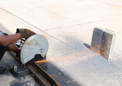 Worker using a metal chop saw to cut steel square tubing with bright sparks flying on a construction site.