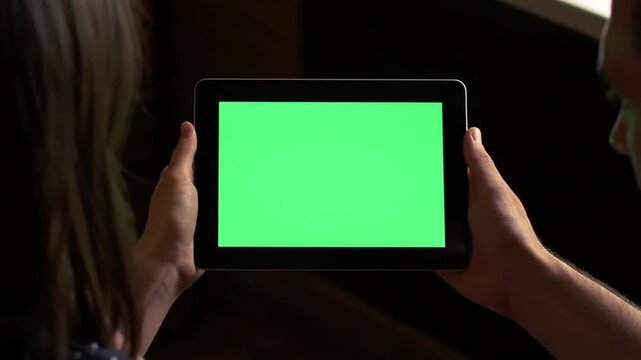 Couple holding tablet with green screen in dark room