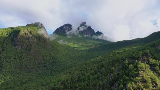 Aerial view of sharp rocky peaks emerging from green misty mountains in Daocheng Yading China