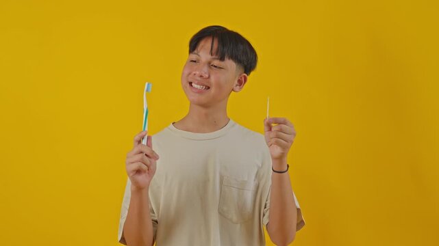 Asian boy holding toothbrush and toothpick against yellow background