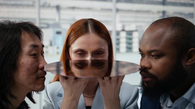 Close up of diverse technicians assessing substrates quality inside factory office, diverse coworkers squinting eyes, studying silicon wafer to improve electronics for semiconductor research.