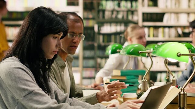 Student pointing at coursework on laptop screen and tutoring session, guidance and academic support for assignment at library study desk.