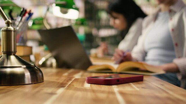 Close up of student using laptop at desk and receives phone message, losing focus and abandoning study session.