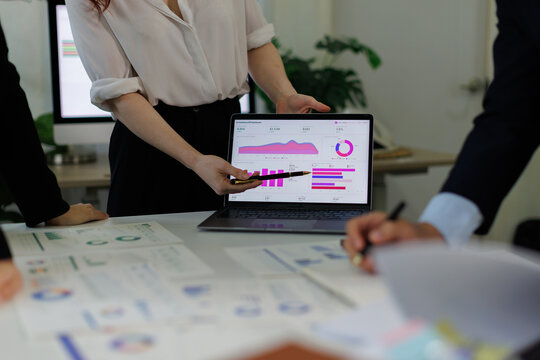 Businesswoman presenting data analytics on a laptop to colleagues during a corporate meeting, showing financial graphs and charts for strategic planning and growth in an office setting