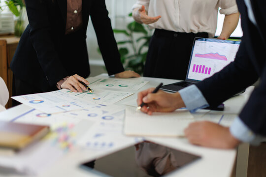Businesswoman presenting data analytics on a laptop to colleagues during a corporate meeting, showing financial graphs and charts for strategic planning and growth in an office setting