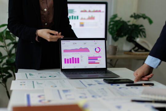 Business professionals analyzing financial data on a laptop and documents, discussing company growth strategies and performance metrics in an office meeting