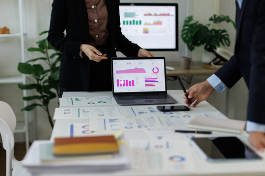 Business professionals analyzing financial performance data on laptop screen, reviewing market charts, discussing economic trends during corporate meeting, planning future growth strategy in office