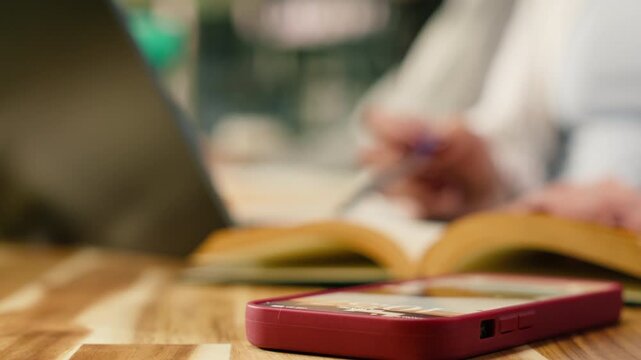 Close up of student using laptop at desk and receives phone message, losing focus and abandoning study session, Digital distraction and addiction to text and browse smartphone, supporting coursework.