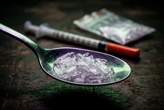 Synthetic drug crystals piled inside a silver metal spoon next to a medical syringe