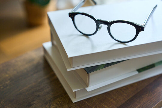 Glasses on stack of books on wooden desk with natural light