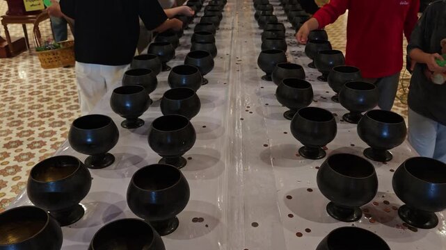 Wide ground-level view of black ritual bowls in double rows on temple floor, coins scattered, worshippers barefoot on Lanna mosaic tiles, Inthakhin merit ceremony, devotional atmosphere