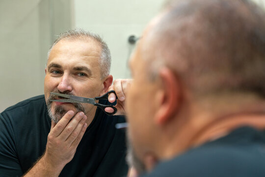 Portrait of Middle-aged handsome man cutting his beard and mooustache with scissors