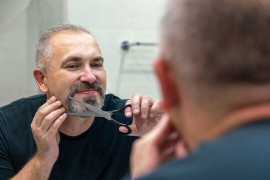Portrait of Middle-aged handsome man cutting his beard and mooustache with scissors
