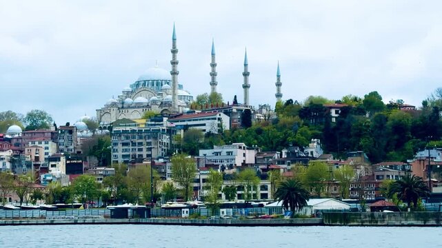 Scenic cityscape view of historic Suleymaniye mosque and New mosque Eminonu with passenger tourist boats sailing on the Bosphorus sea water in cloudy weather.