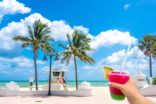 Seafront beach promenade with hand holding cocktail and palm trees on background on sunny day in Fort Lauderdale in Florida USA