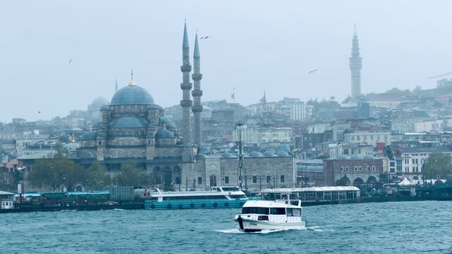 Scenic view of the historic New Mosque Eminonu with minarets and domes, passenger tourist boats sailing on the Bosphorus, and seagulls flying in cloudy weather.