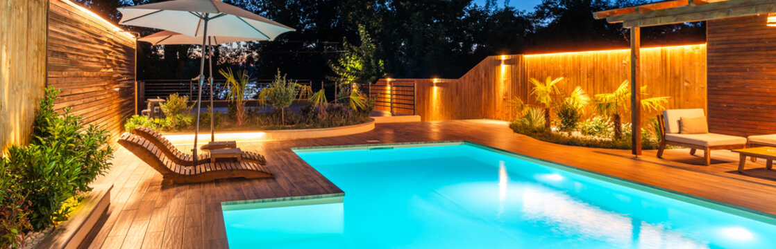 Luxury swimming pool with wooden deck and cozy lighting at night. Concept of relaxing outdoor living space