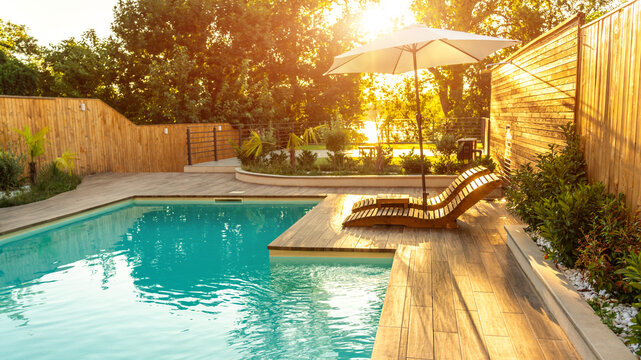 Swimming pool in modern private villa with lounge chairs, palm trees and umbrella