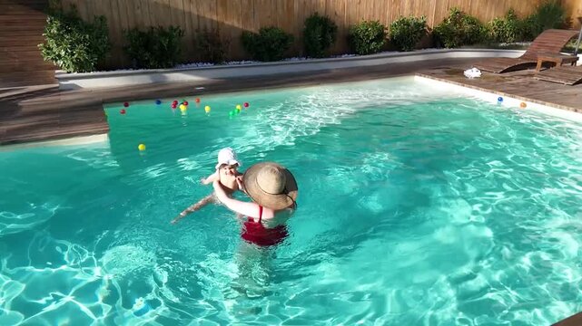 Mother and baby enjoying playtime in outdoor swimming pool surrounded by greenery on a sunny day