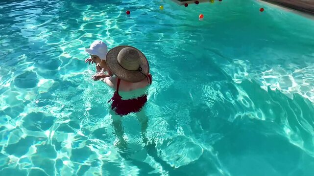 Mother and baby enjoying playtime in outdoor swimming pool surrounded by greenery on a sunny day