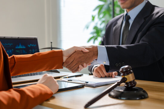 Business handshake across a desk with a judge gavel in focus, suggesting legal agreement, mediation, contract signing, or successful case resolution in a modern office.