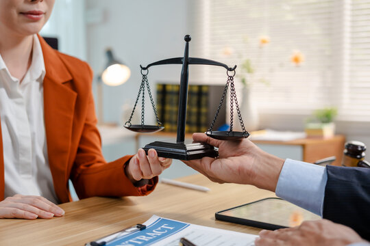 Lawyer and client holding balance scales across an office desk, with contract papers and tablet nearby, showing legal advice, justice, trust and business agreement.