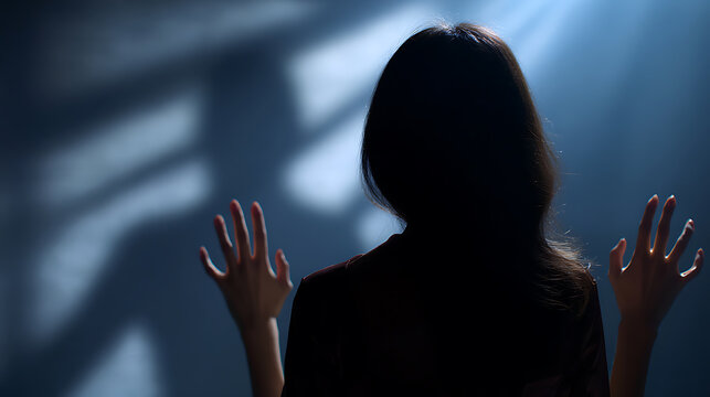 A woman stands with her back to the viewer, hands raised, bathed in a dramatic spotlight with shadow patterns on a dark background