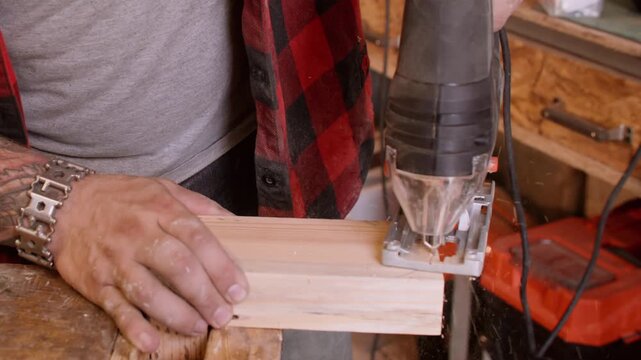 Carpentry occupation. Furniture making. Craftsman hand with professional jigsaw cutting wood plank corner in curve line on workbench with sawdust.