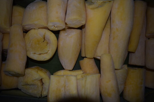 A close-up shot of raw, peeled, and sliced yellow cassava roots stacked together, ready for traditional food processing or boiling.