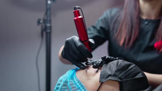 Cosmetologist applies permanent makeup on eyebrows with modern machine.