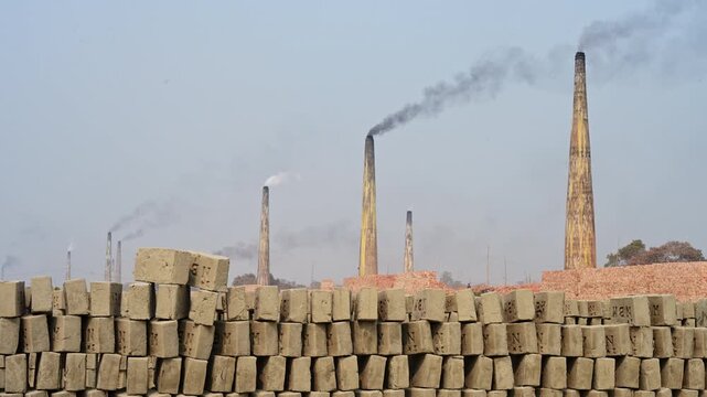 Industrial kiln chimneys emit black smoke over drying brick rows in Bangladesh. Captures severe air pollution, environmental degradation, carbon emissions, and climate change impact in Dhaka.