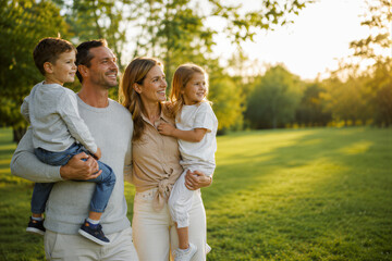 Fototapeta premium Parents Carrying Their Children in Sunny Park with Copy Space