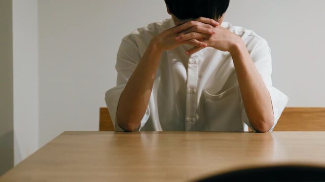Person in White Shirt Hiding Face Behind Hands at Wooden Desk