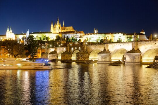 Night scenery of Charles Bridge with the majestic Prague Castle and St. Vitus Cathedral in background at blue dusk and reflections of lights on the water of Vltava River, in Old Town Prague, Czech