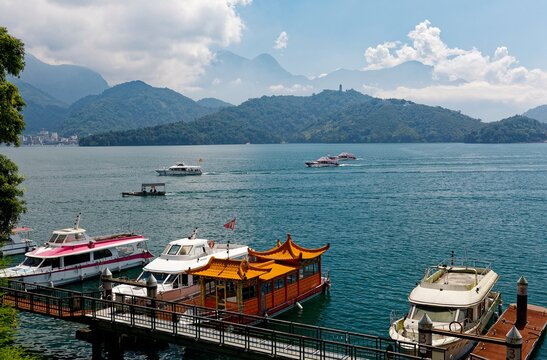 Scenery of boats and yachts moored to the docks at Shuishe Pier on a sunny summer day and high-rise hotels standing on the lakeside hill of Sun-Moon Lake, a popular tourist resort in Nantou, Taiwan