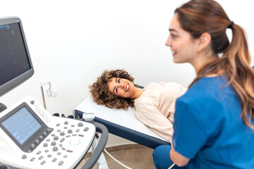 Obraz premium A smiling female patient lies on an examination table while a doctor performs an ultrasound scan. Modern diagnostic healthcare equipment, clinical checkup procedure, and professional medical services.
