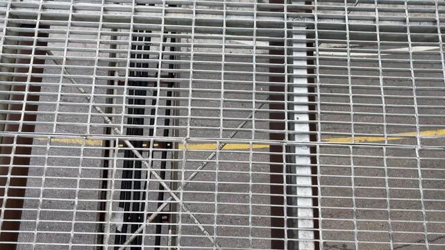 Point of view (POV) of feet in sandal walking on an elevated pedestrian skywalk made of steel grating panels during a bright day.