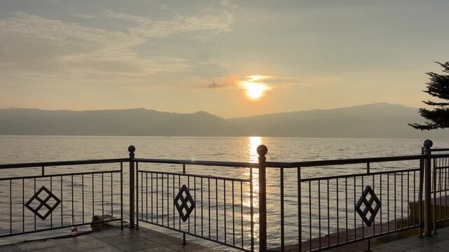 Panoramic time-lapse of a sunset at Lake Toba with a traditional Batak style resort terrace in the foreground, bright sunrays cutting through clouds