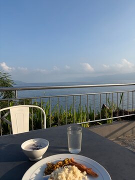 A beautiful resort breakfast setup featuring pastries, and ice water, overlooking a peaceful blue lake under a clear sky