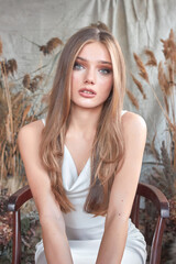 Fototapeta premium A young woman with long, wavy brown hair and expressive blue eyes. She is wearing a white sleeveless top and is looking directly at the camera.