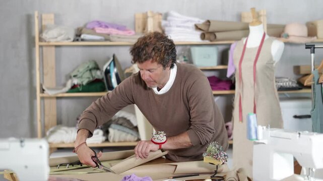 Adult male fashion designer stands near a table and cuts paper in a sewing workshop. Tailor makes patterns and plans to sew clothes. High quality 4k footage